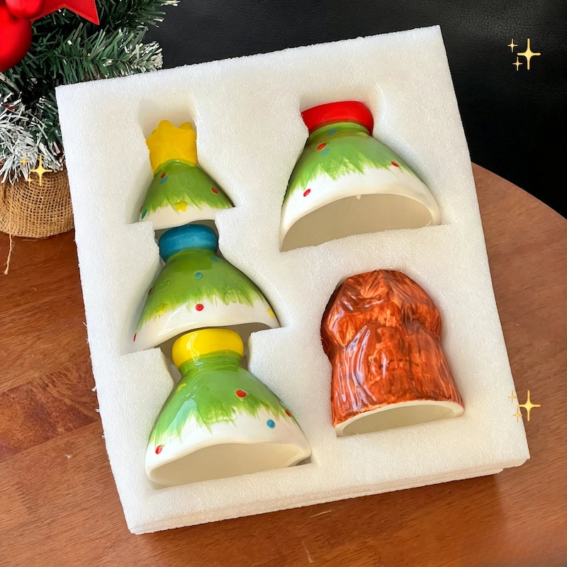 Hand holding green ceramic Christmas tree cup in front of a holiday wreath